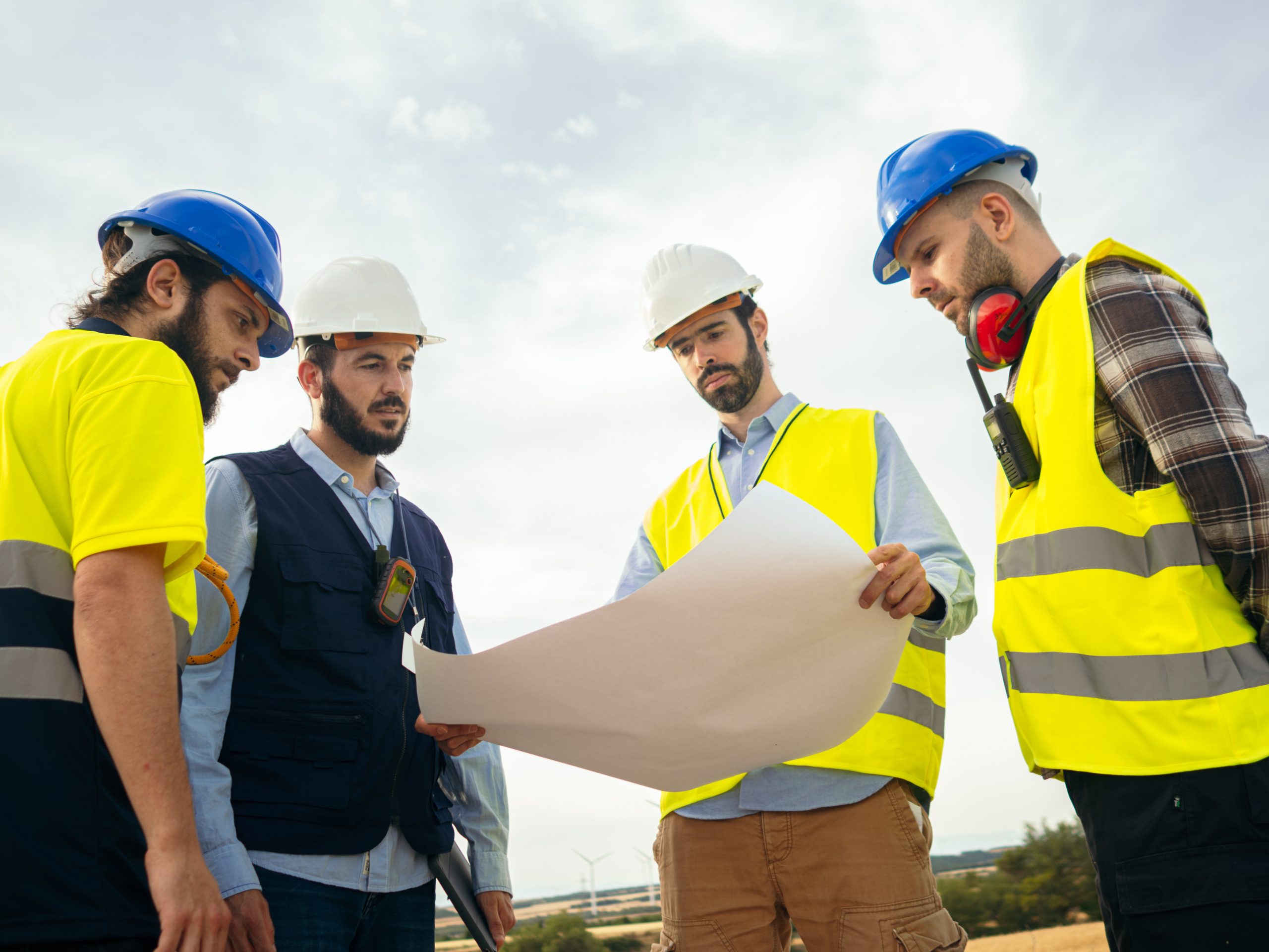 Group of Caucasian male engineers looking at a blueprint in a windmill park