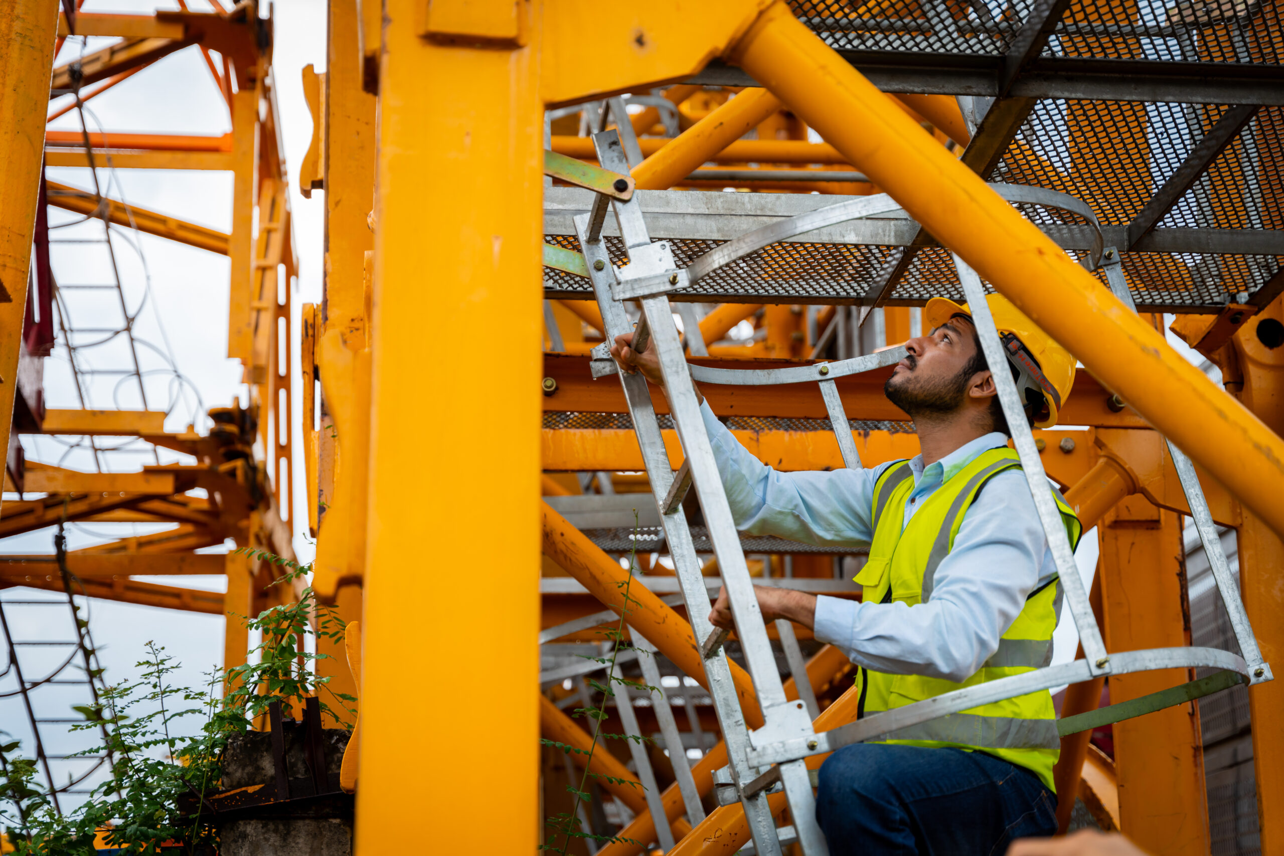 A man in a yellow vest is climbing a ladder to reach a high spot