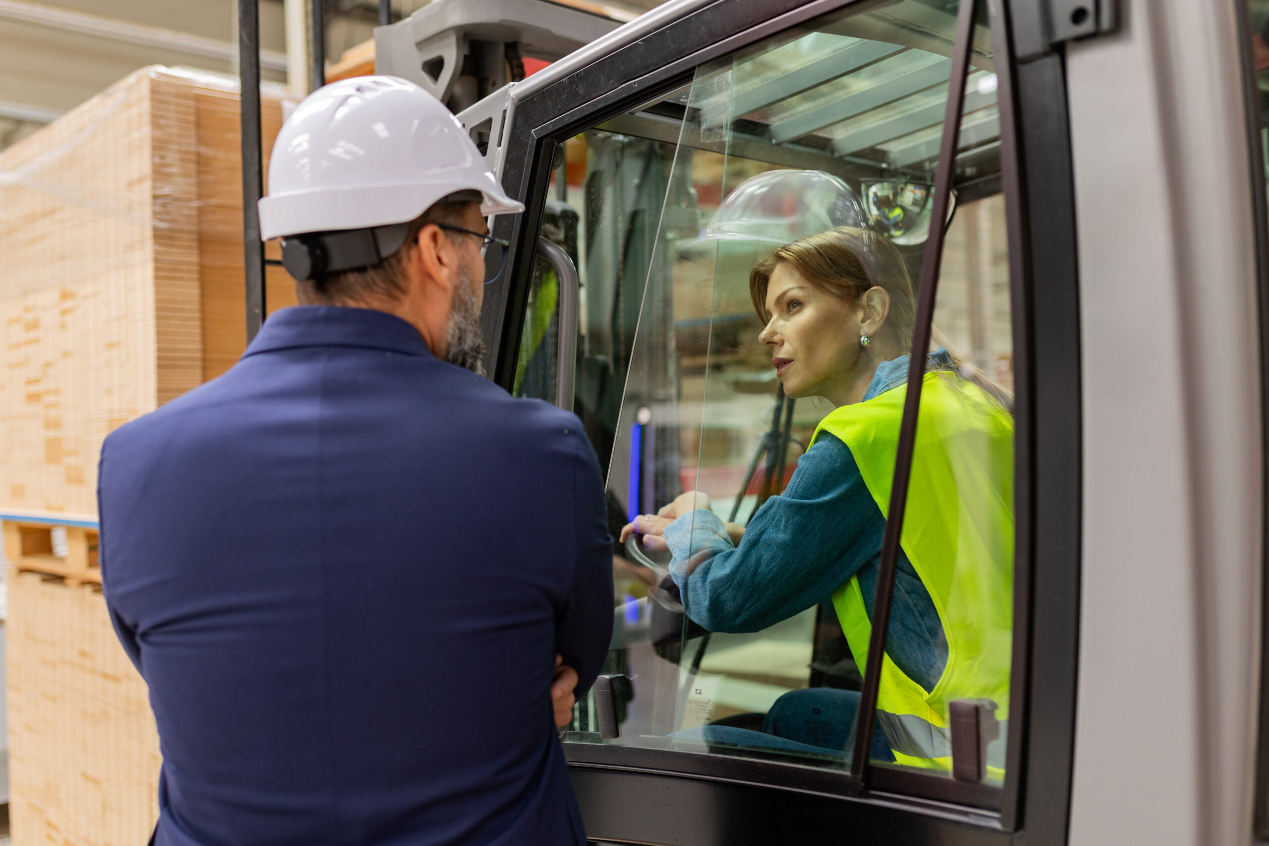Female forklift driver talking with manager in warehouse, order picking. Warehouse worker preparing products for shipmennt, delivery, checking stock in warehouse.
