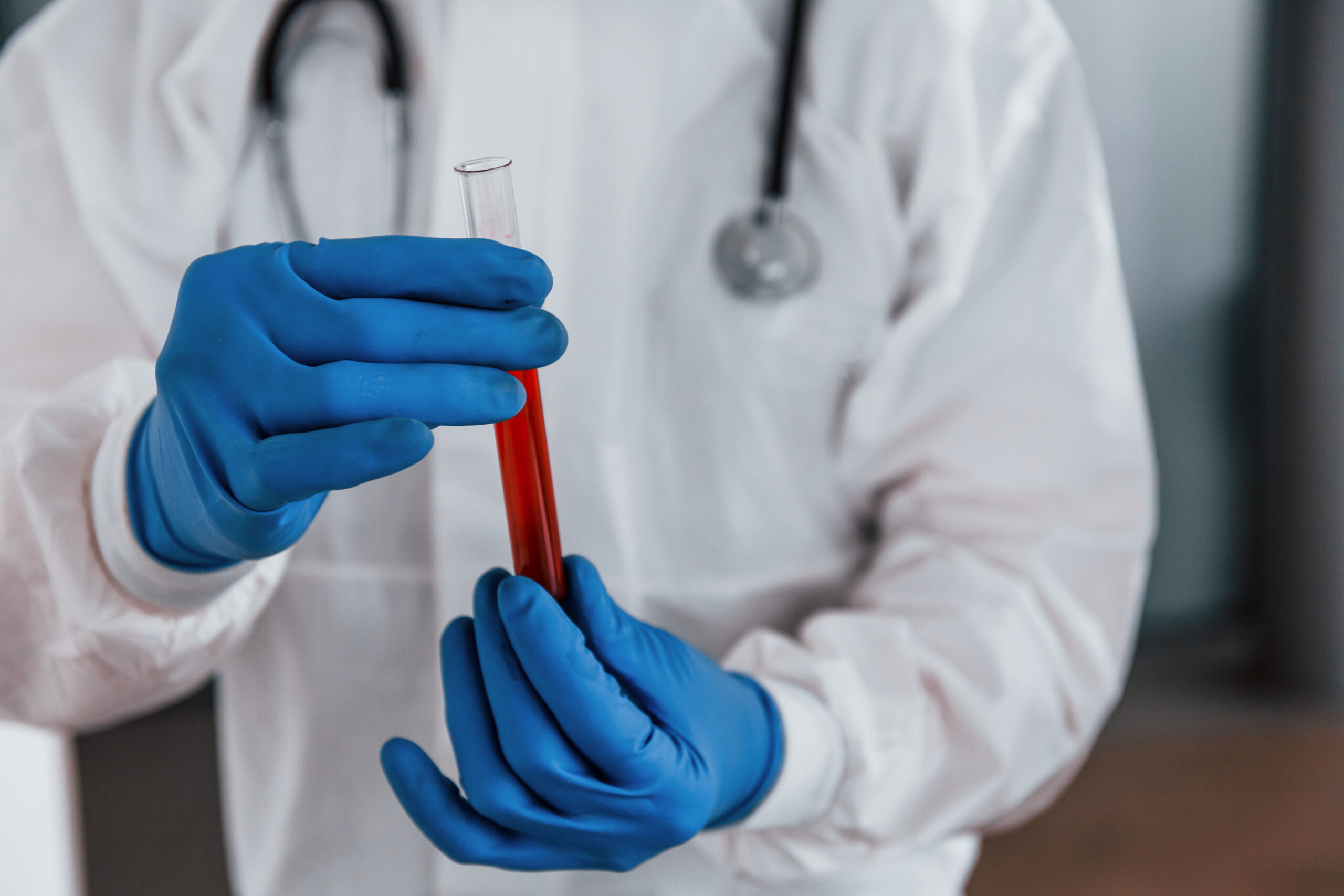 Male doctor scientist in lab coat, defensive eyewear and mask holds test tube with blood