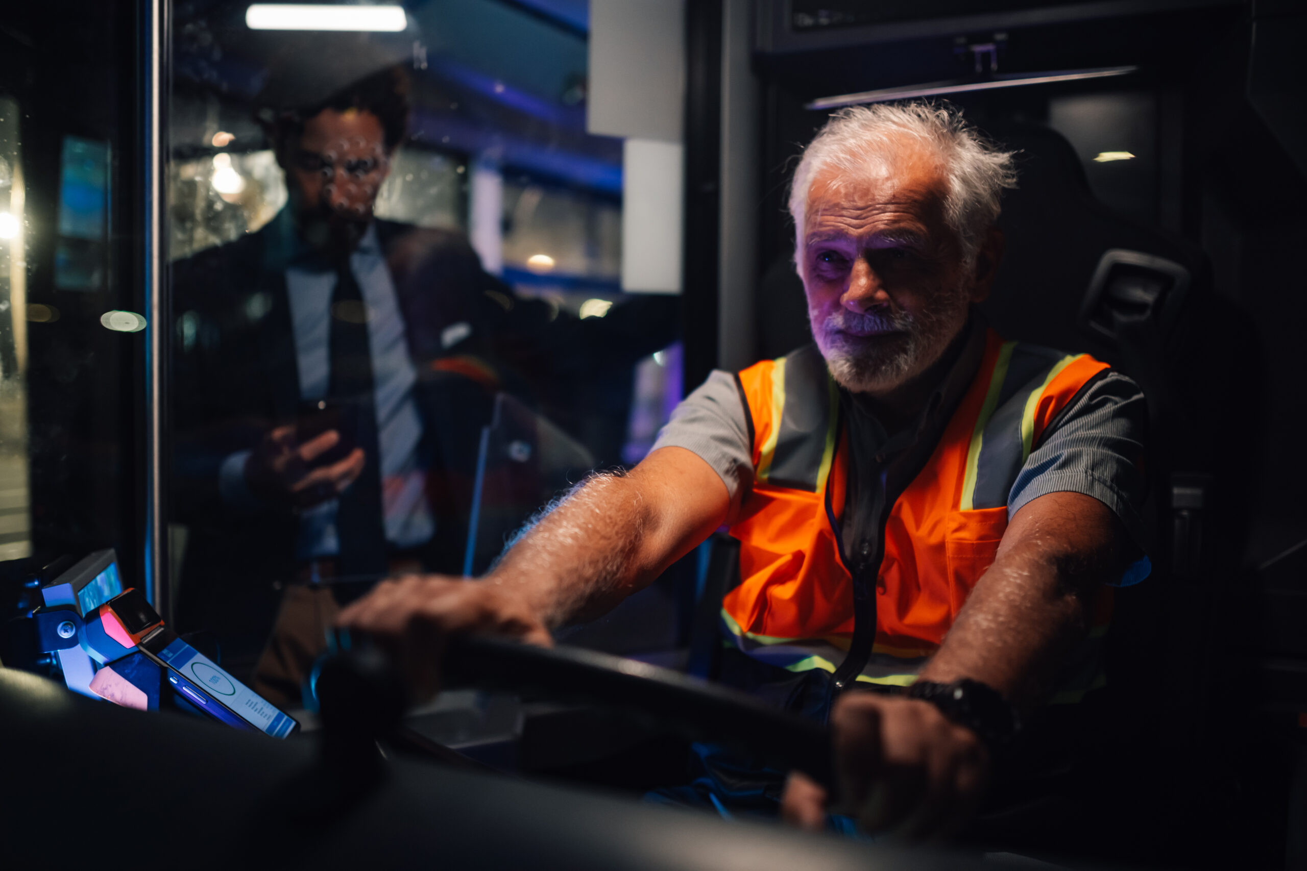 Senior bus driver steering wheel, driving at night, passenger boarding