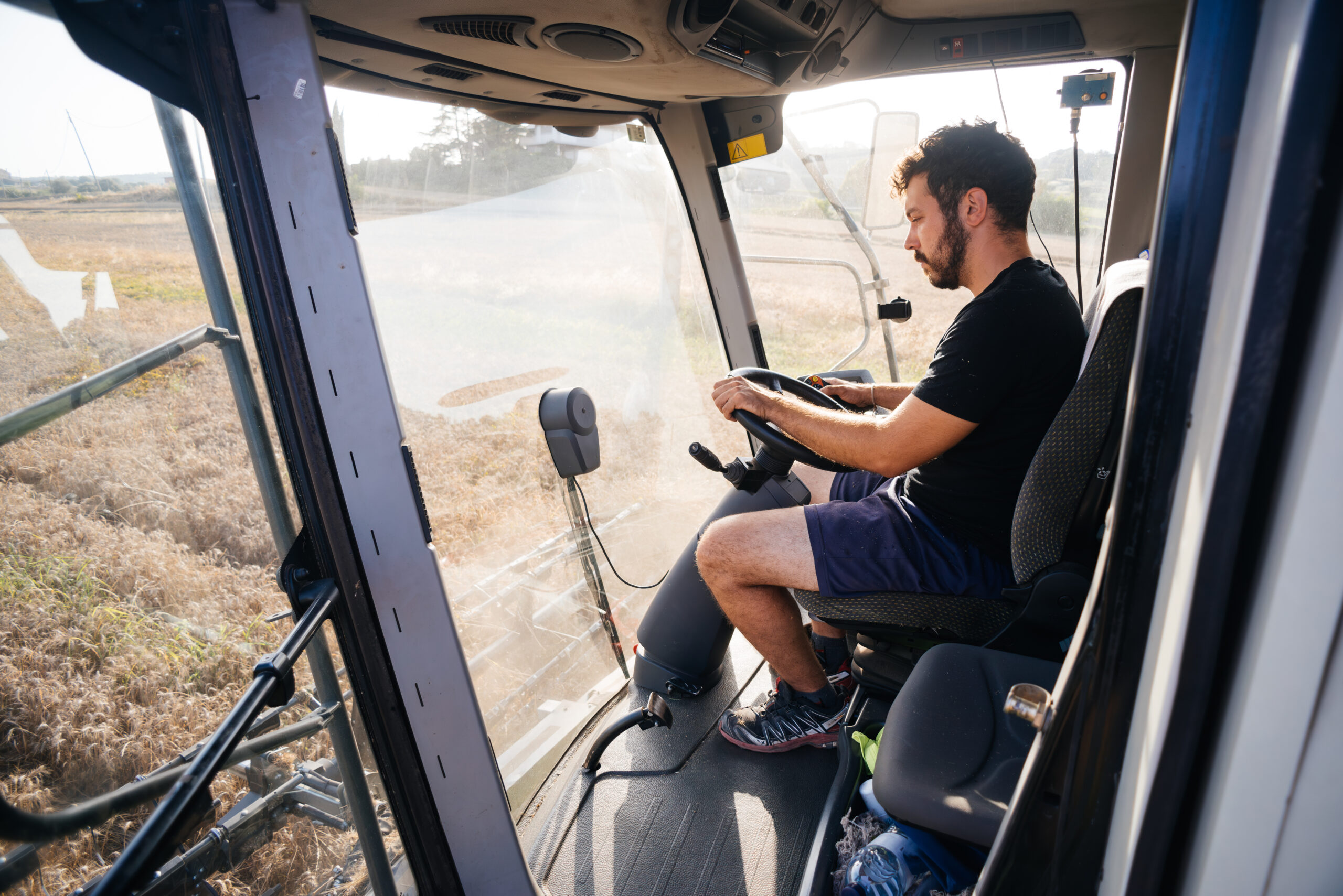 Young bearded man driving harvester in wheat field during daytime