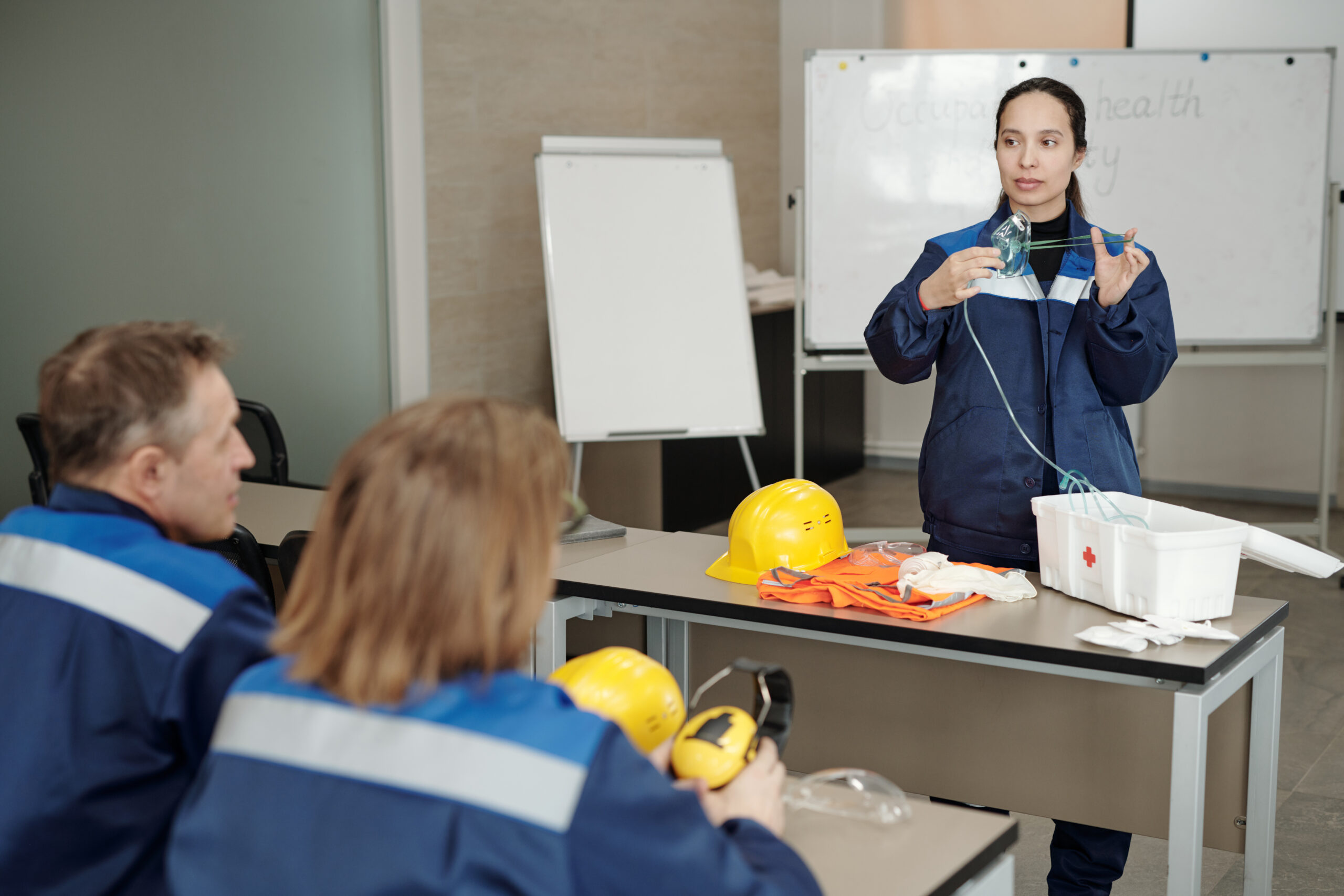 Young female worker demonstrating usage of respirator while standing by desk in front of colleagues