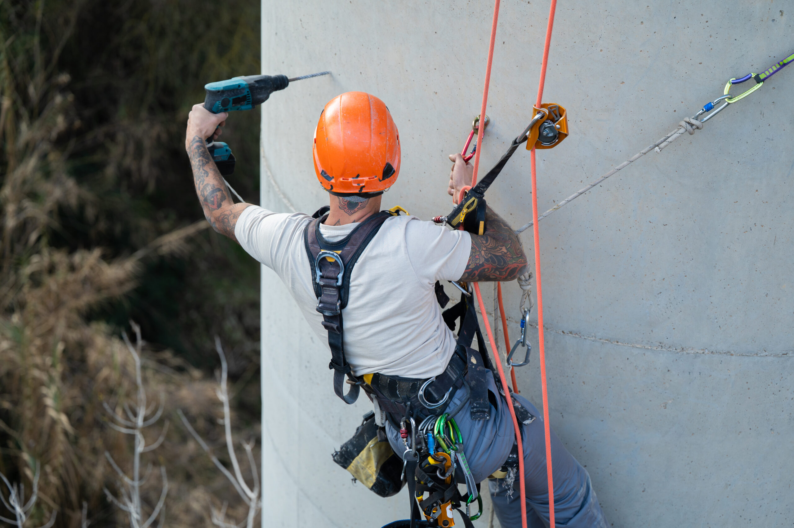 Rope access technician using rotary hammer drill on concrete chimney