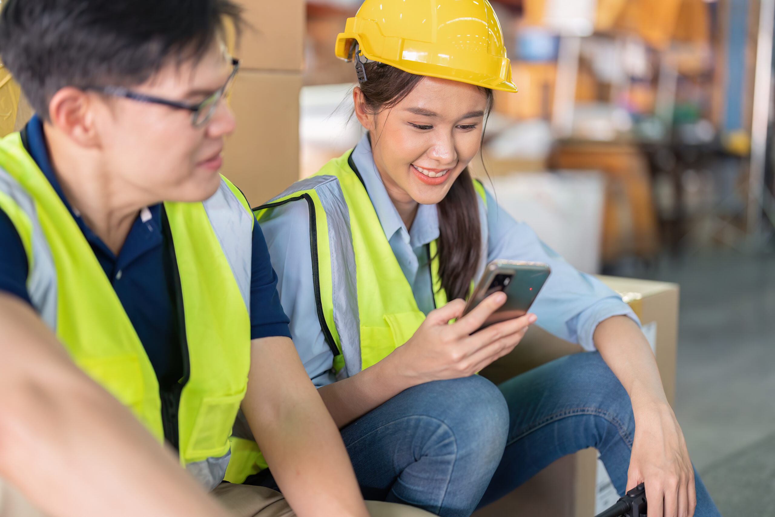 Staff in large storage warehouse together sit back relax funny laughing check mobile phone