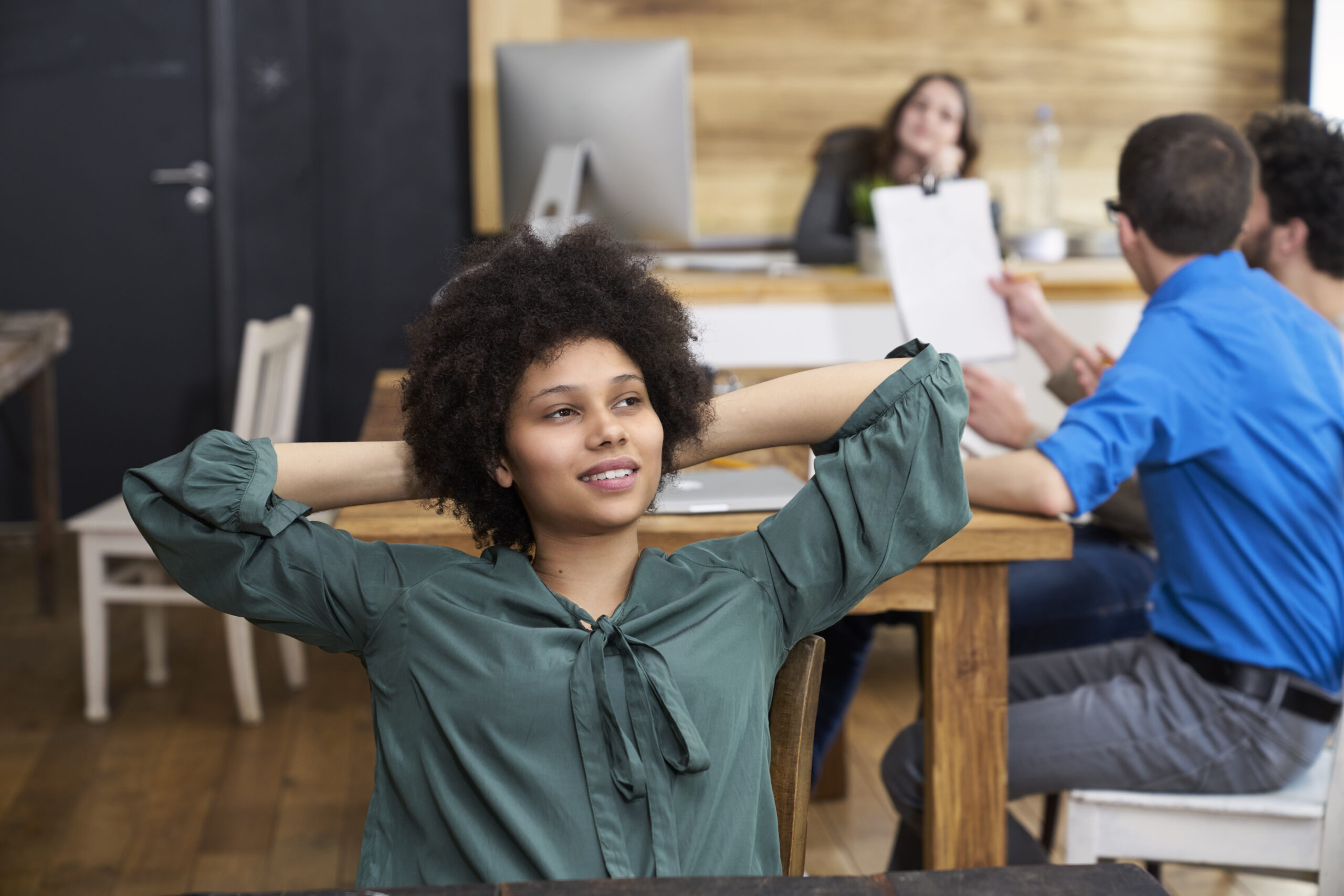 Young woman thinking in office with coworkers in background