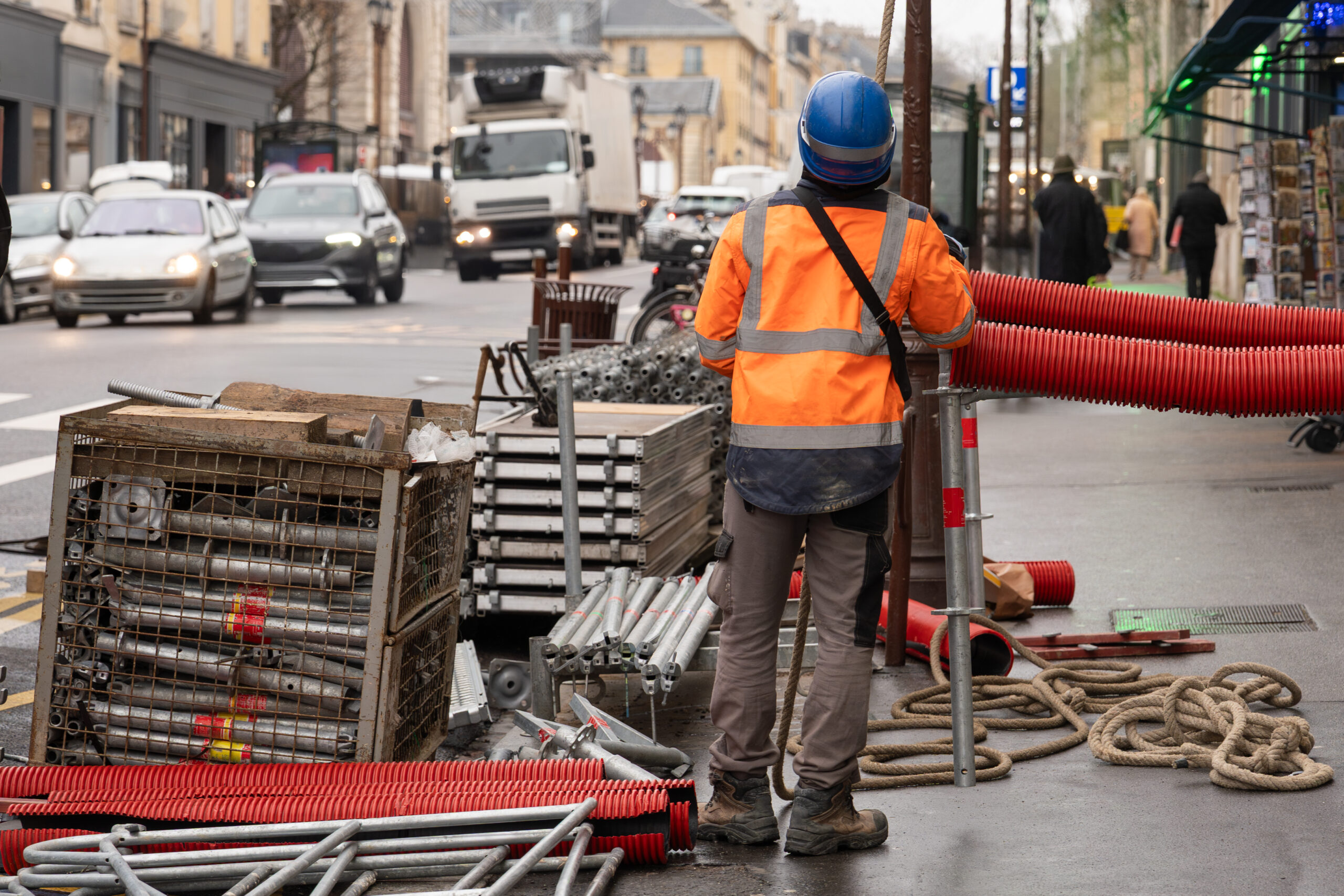 A worker in a hard hat sets up scaffolding on a busy street in the city center.