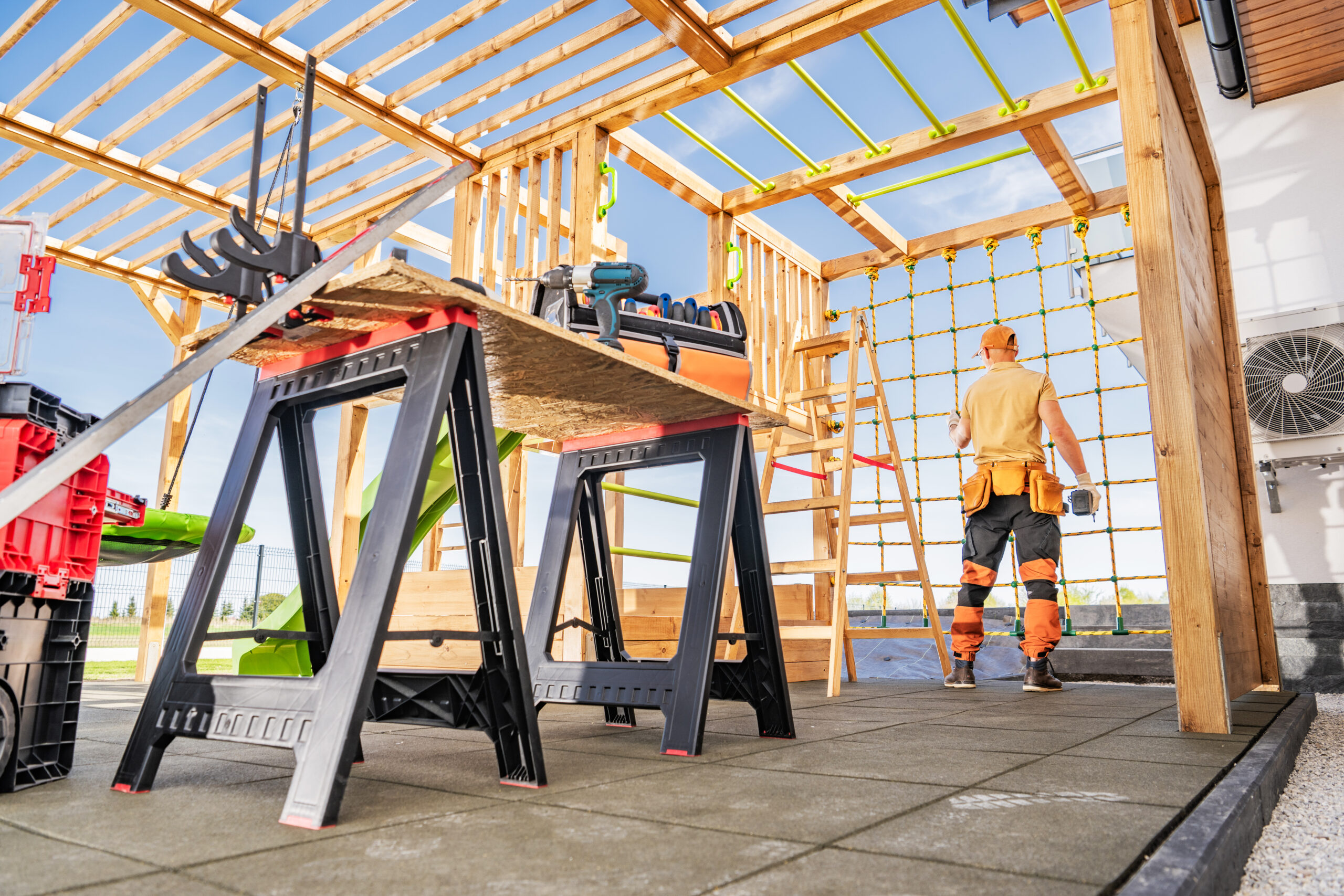 Construction Worker Focuses on Building a Wooden Structure at a Job Site Under Clear Blue Skies During Daylight Hours